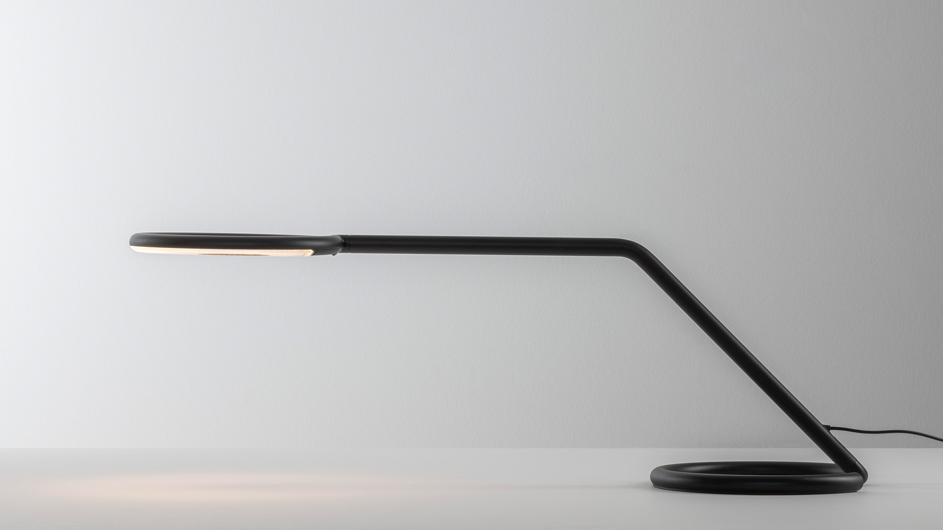 Artemide Vine Light: slim black floor lamp with sinuous arm and circular LED ring head, casting elegant shadow on white wall corner