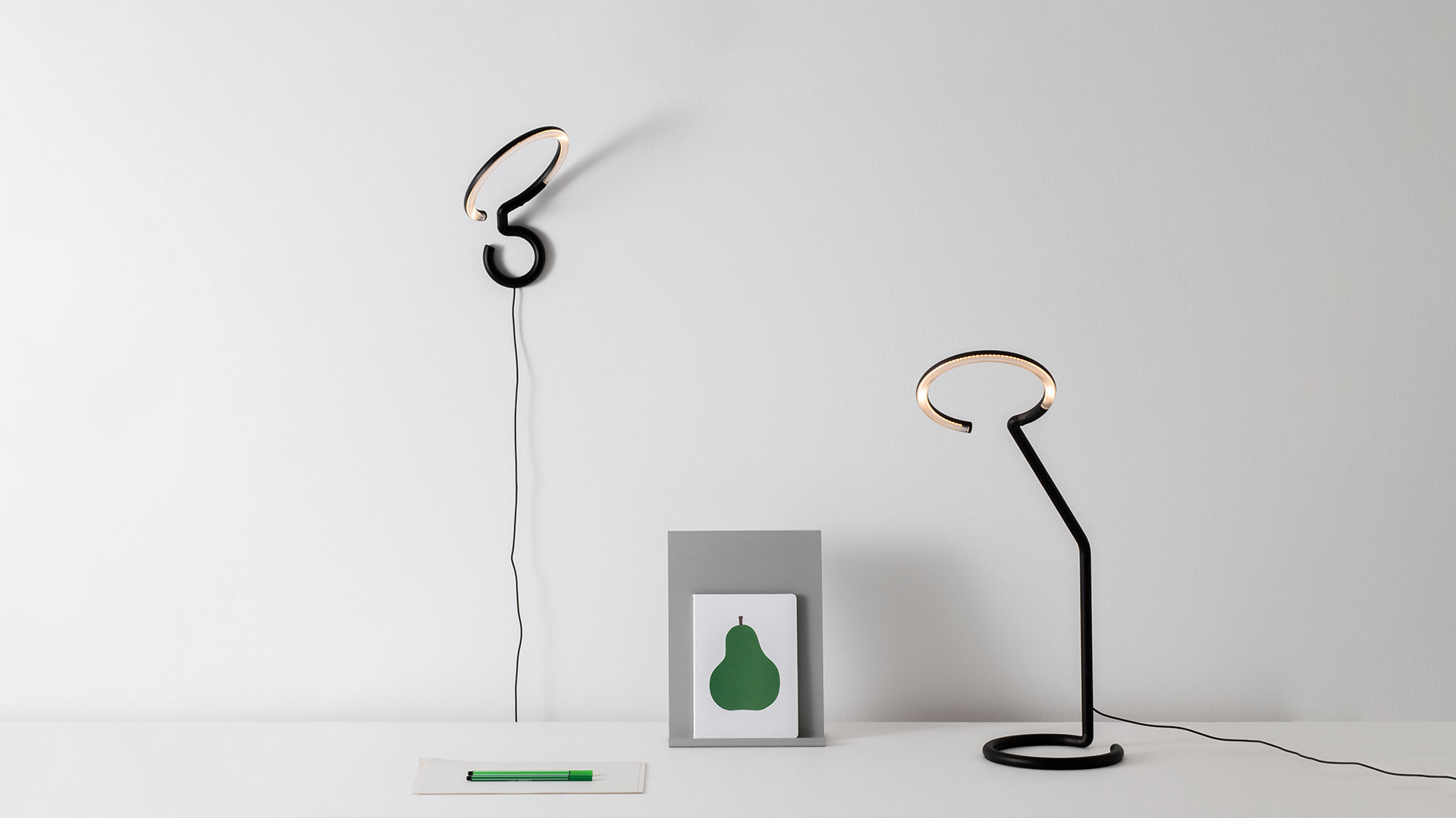 Artemide Vine Light desk lamp in black, featuring a slender angled arm with a circular LED ring head resting on a flat round base.
