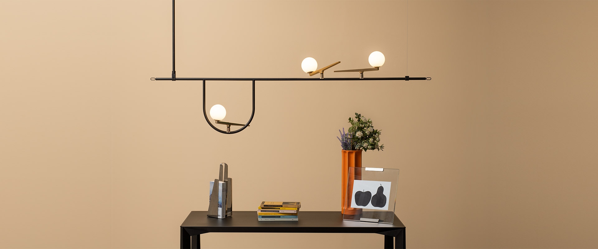 Artemide Yanzi pendant lamp: black horizontal bar with brass joints and three opal globe lights, suspended above a dark console table