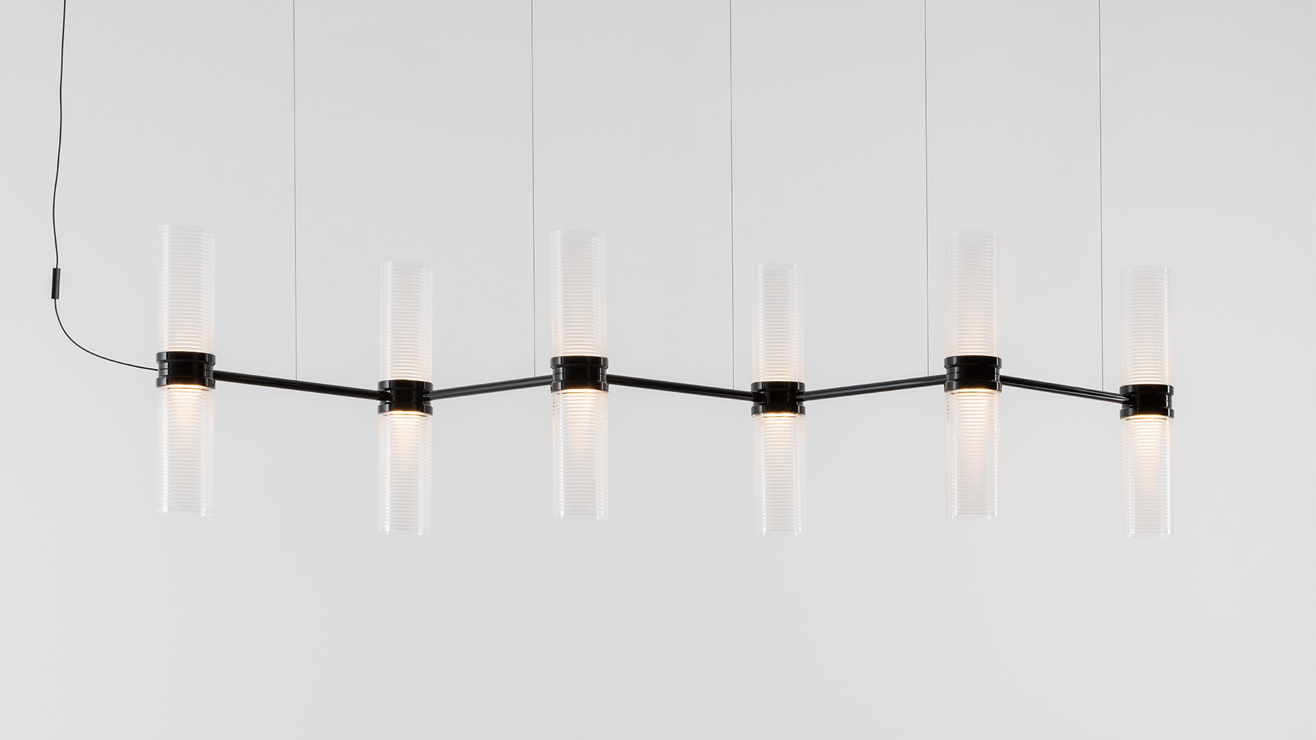 Artemide Zephyr pendant chandelier with six cylindrical ribbed glass diffusers on a horizontal metal arm, suspended outdoors.